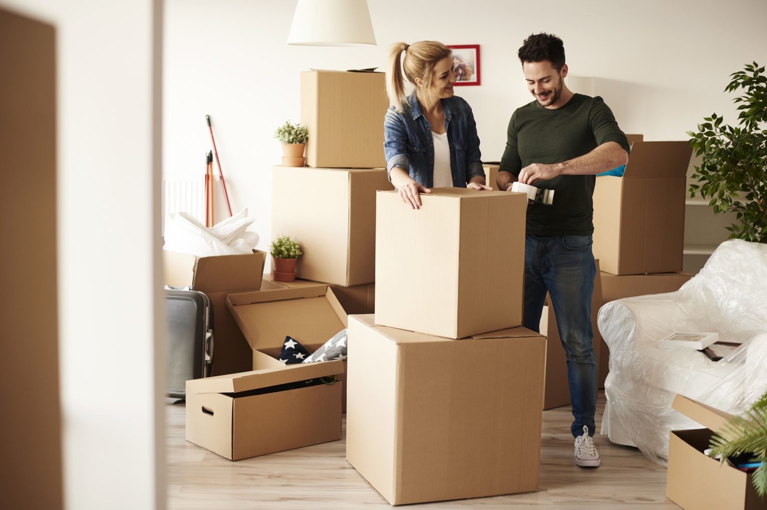 Couple packing household items into cardboard boxes in their living room